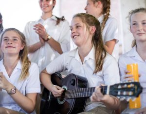 New grade 8 high school students, playing music together, with a girl playing a guitar in the middle