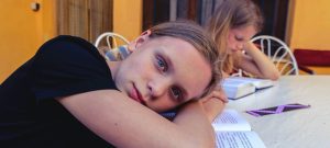 A sleepy school age child lying on her book, indicating she is tired