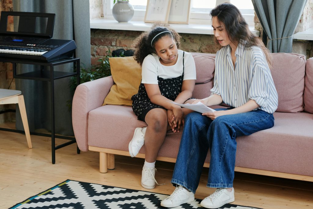 Private Tutor alternative and student sitting on a sofa at home, reviewing a worksheet together in a bright living room.